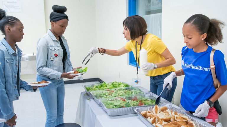 two young girls are served a healthy plate of salad by two service workers
