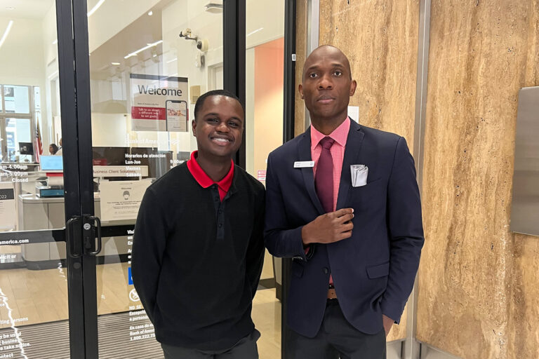 a young intern stands in front of an office entrance with his older mentor