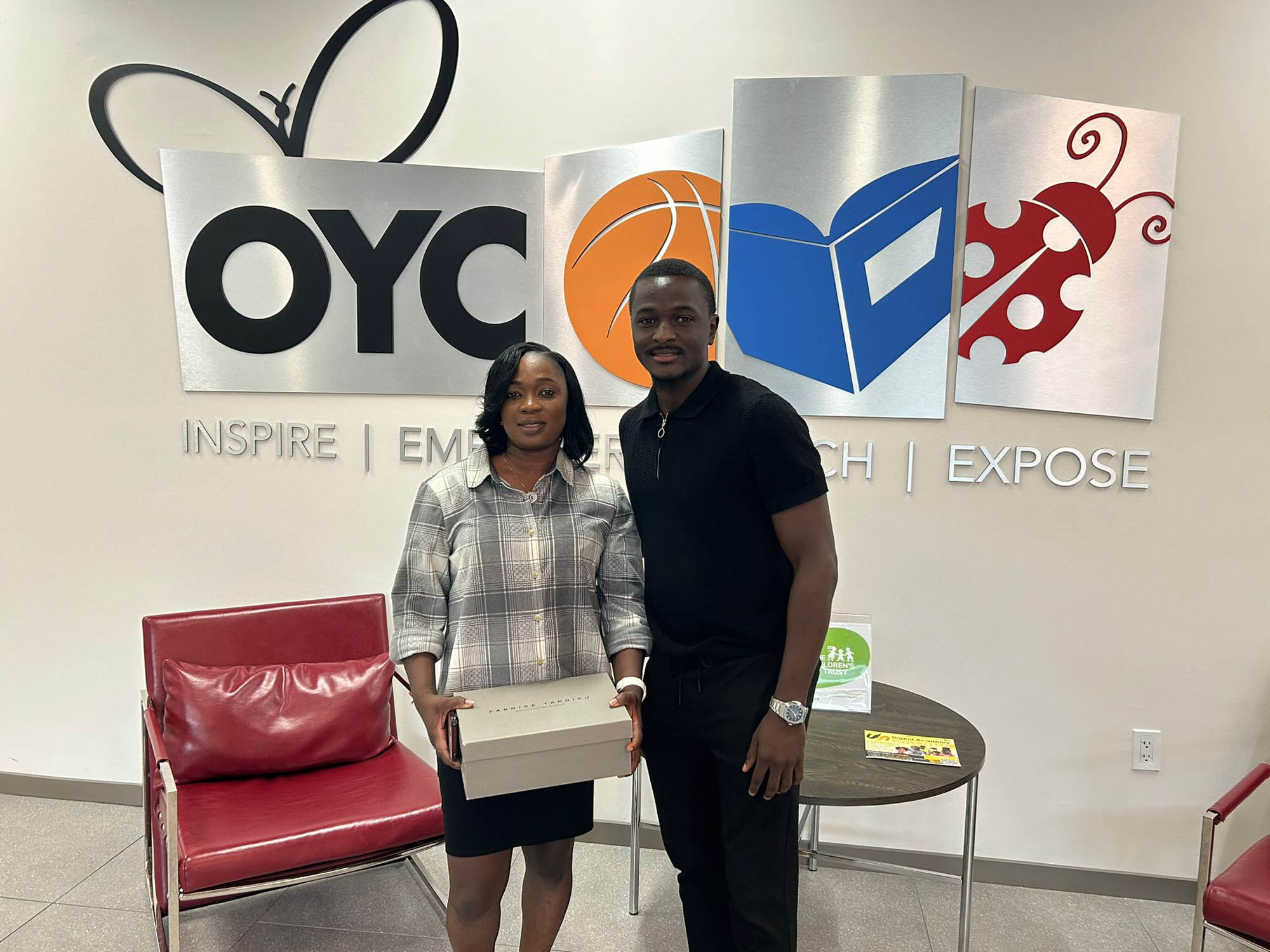 a man and a woman stand in the OYC lobby while holding a box of shoes.
