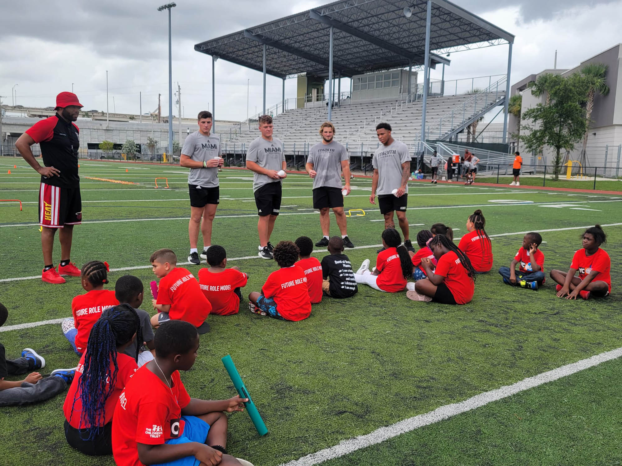 4 players from the University of Miami give a group of young boys some pointers about playing football.