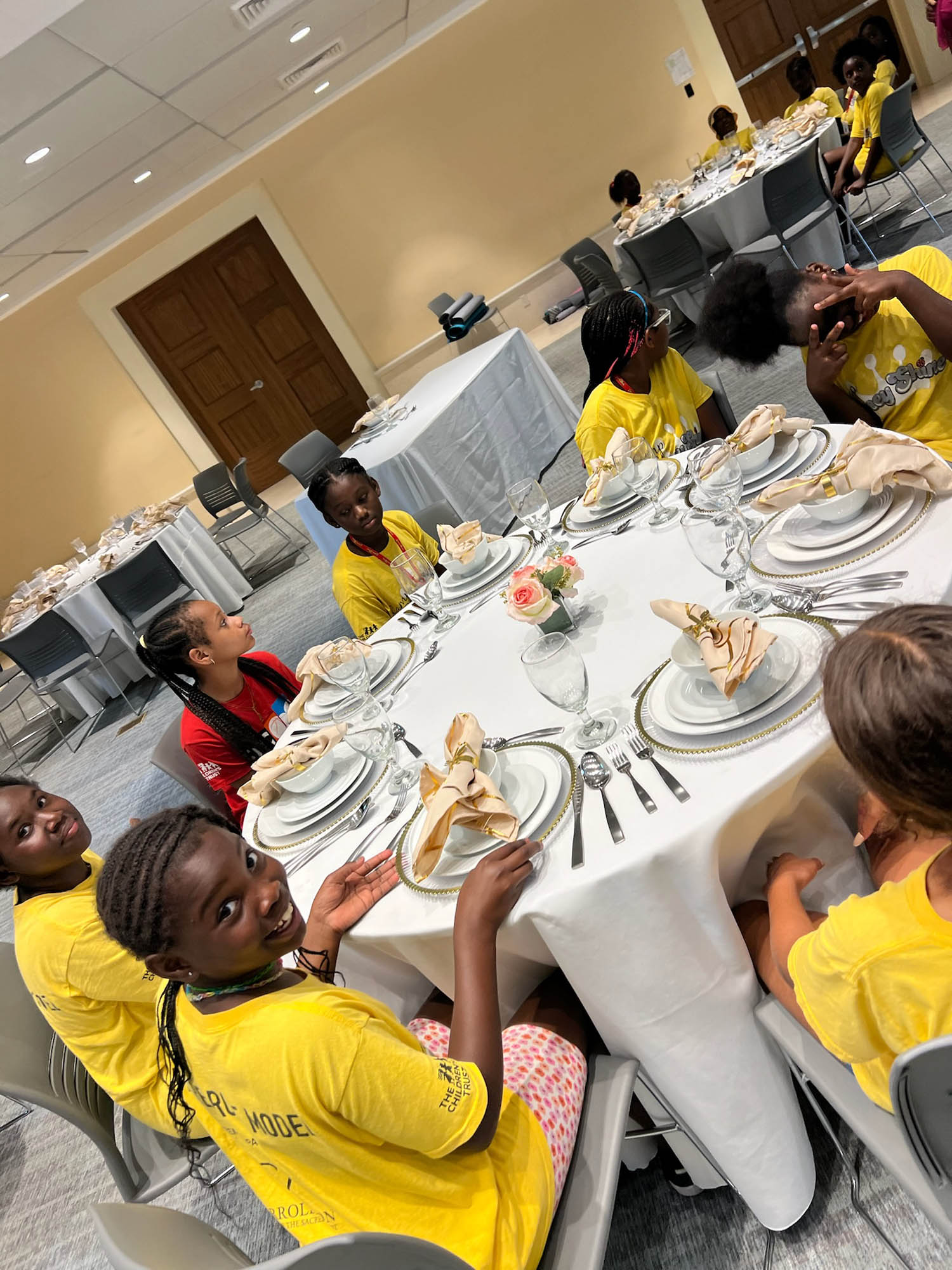 a group of young girls seated at a round table learn proper placement of silver and stem ware.