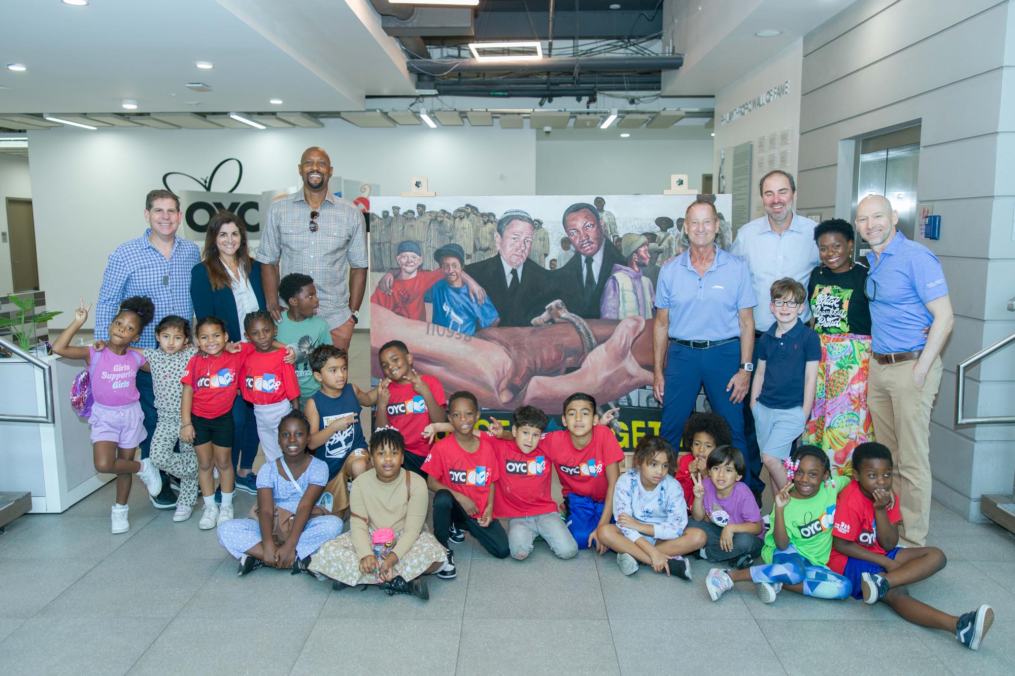 a group of people pose for a photo. They are surrounding a painting by Alonzo Adams.