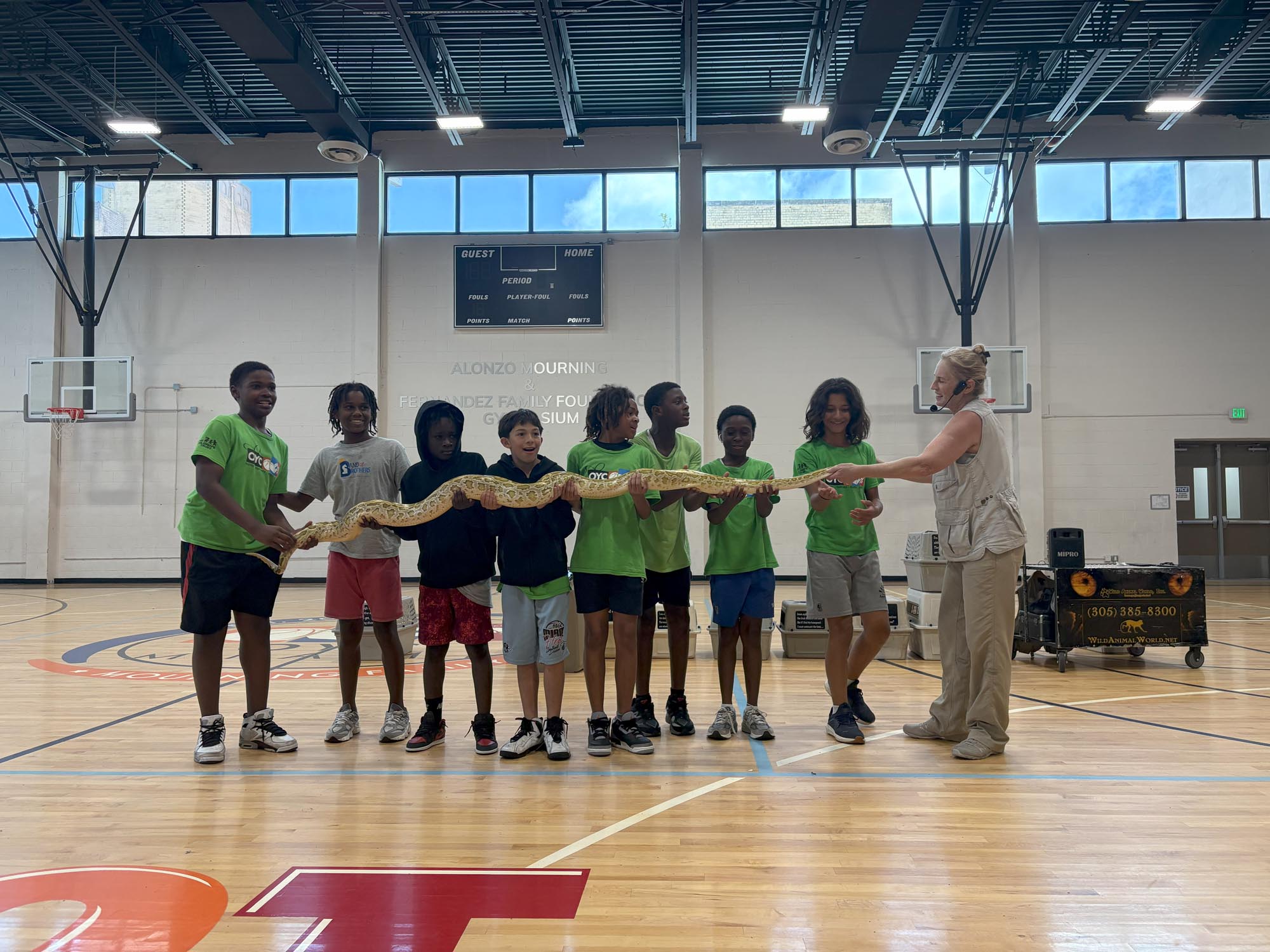 a group of children hold a large constrictor snake inside a gymnasium