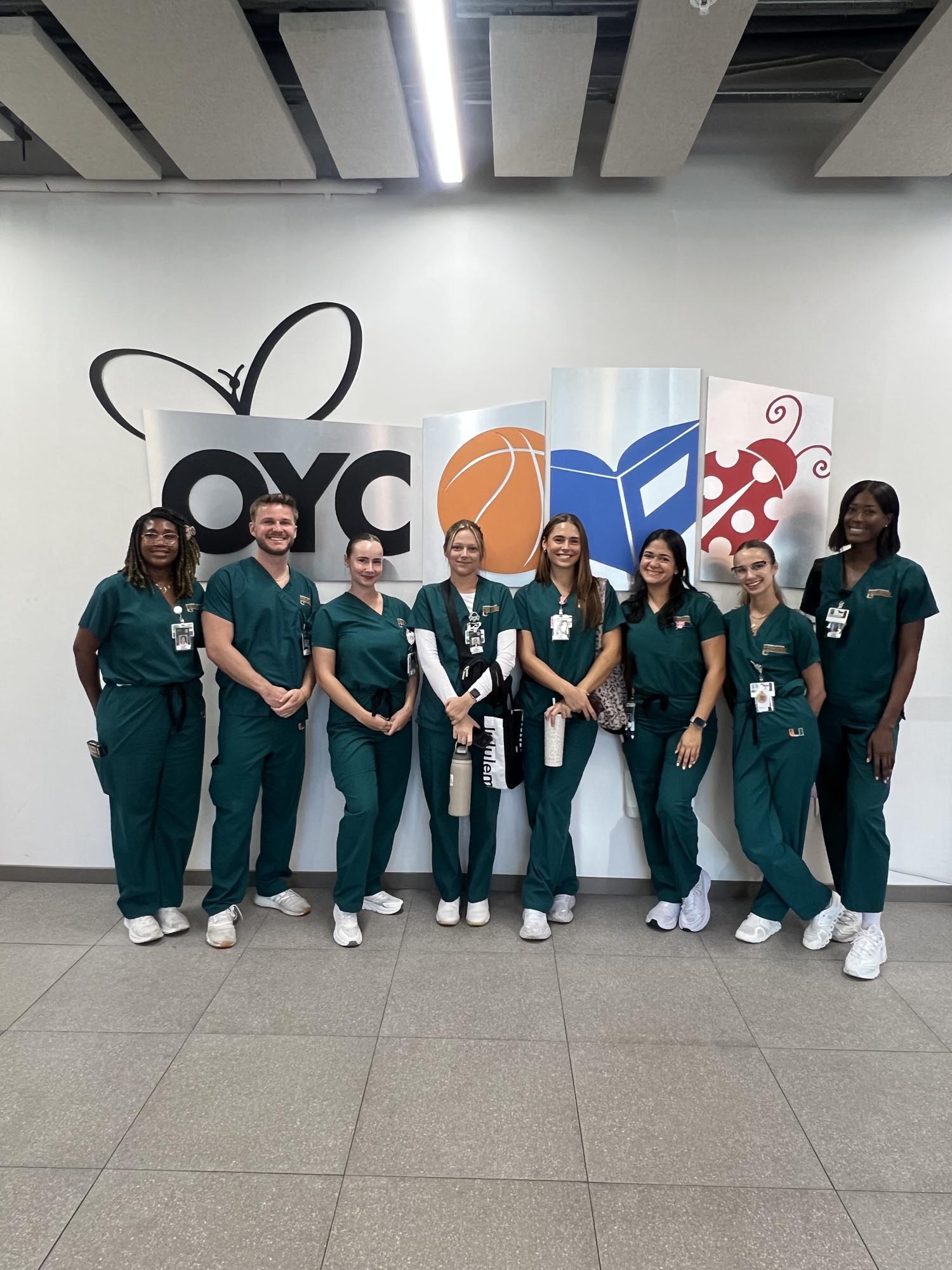 a group of volunteers poses for a photo in front of an OYC Miami sign