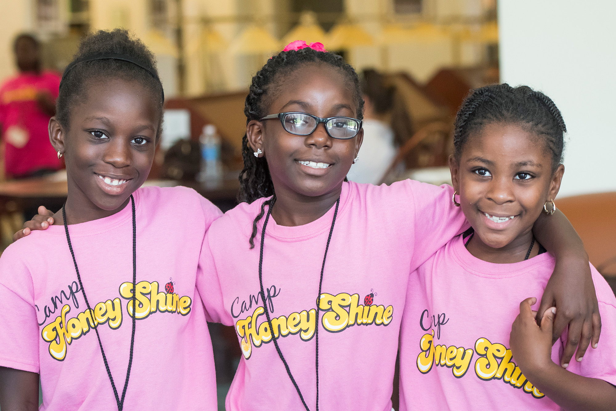 3 young girls wearing pink tees stand arm in arm