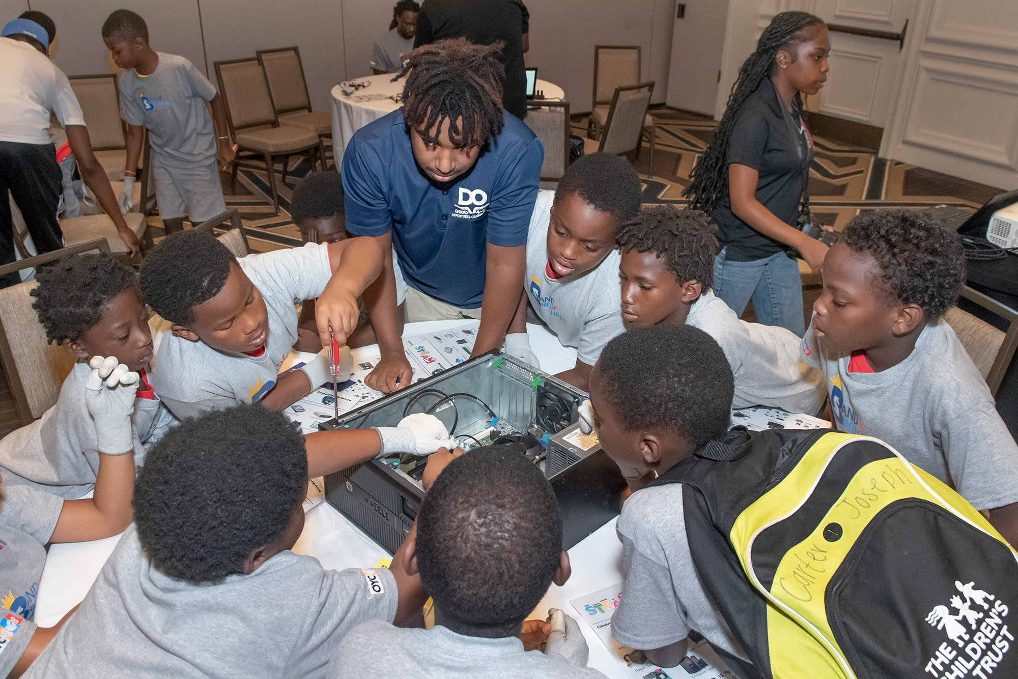 a group of young boys and a young man work on a computer at a table