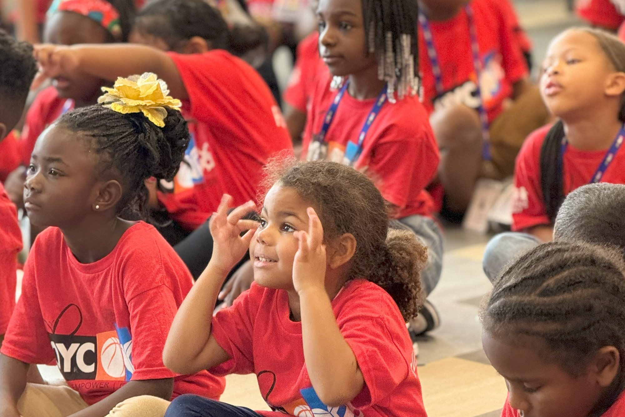 young girls in a gymnasium attentively watch a speaker's presentation