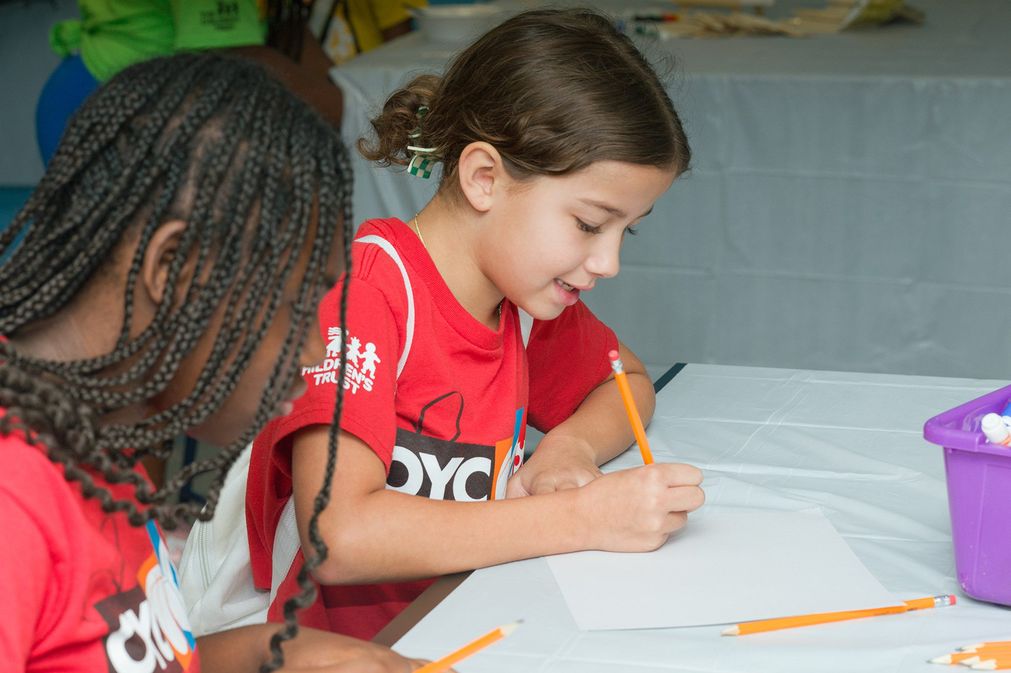two young girls sit at a table and do their homeowrk
