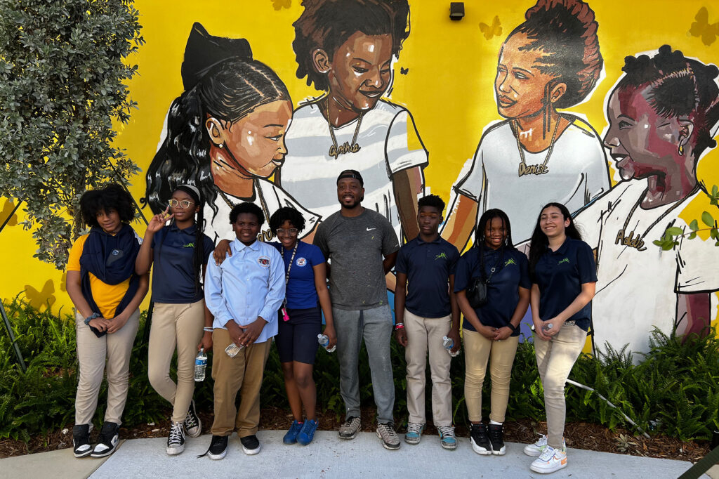 a group of middle school students stands in front of a mural on the outside of a building