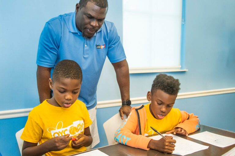a mentor helps two young boys with their assignments