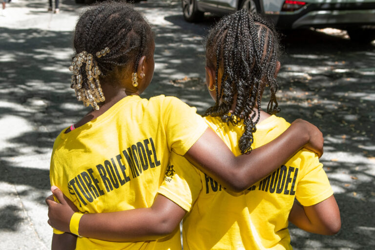 rear view of two young girls wearing yellow shirts standing arm in arm