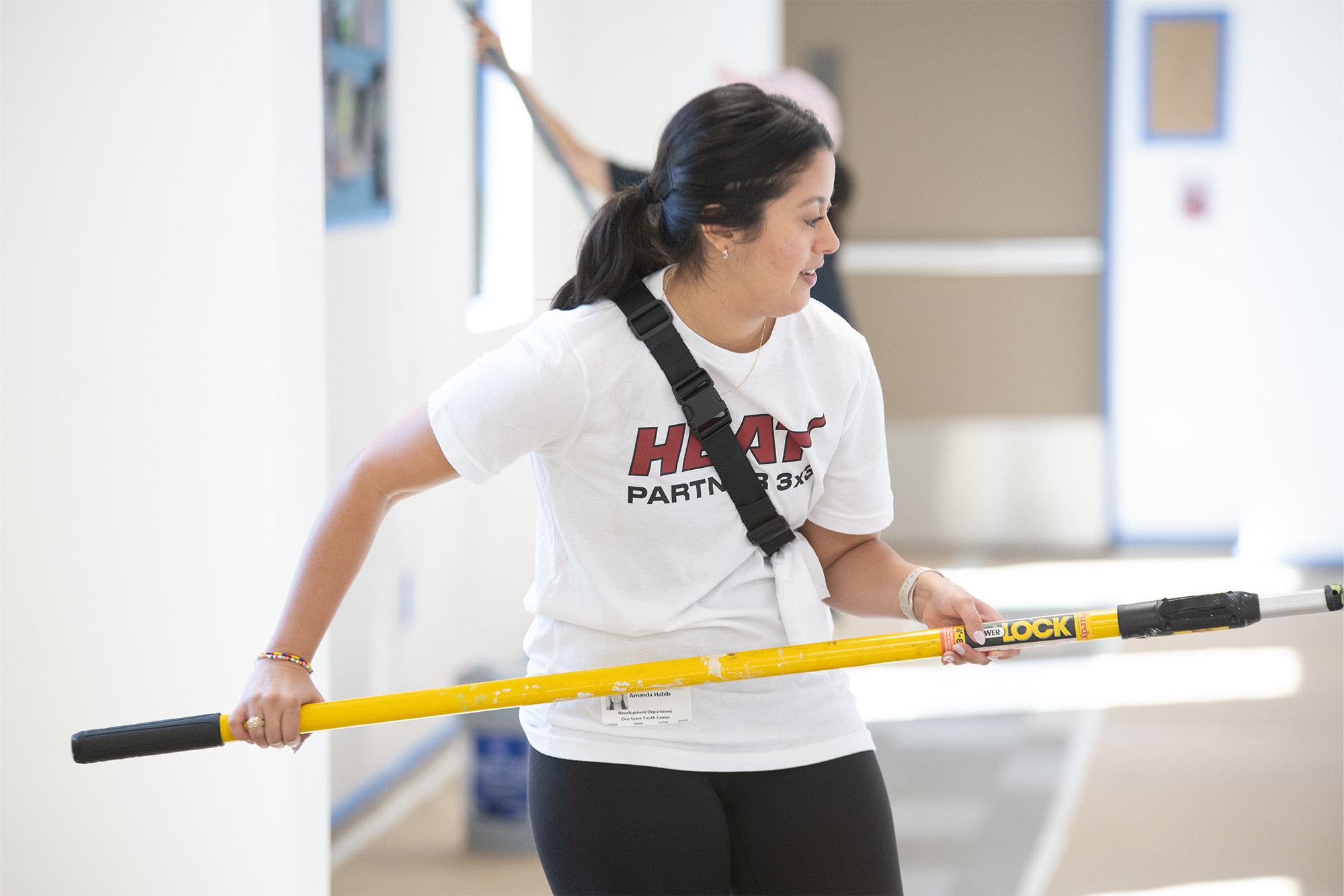 a woman wearing a Miami Heat tee-shirt uses a paint roller inside a hallway