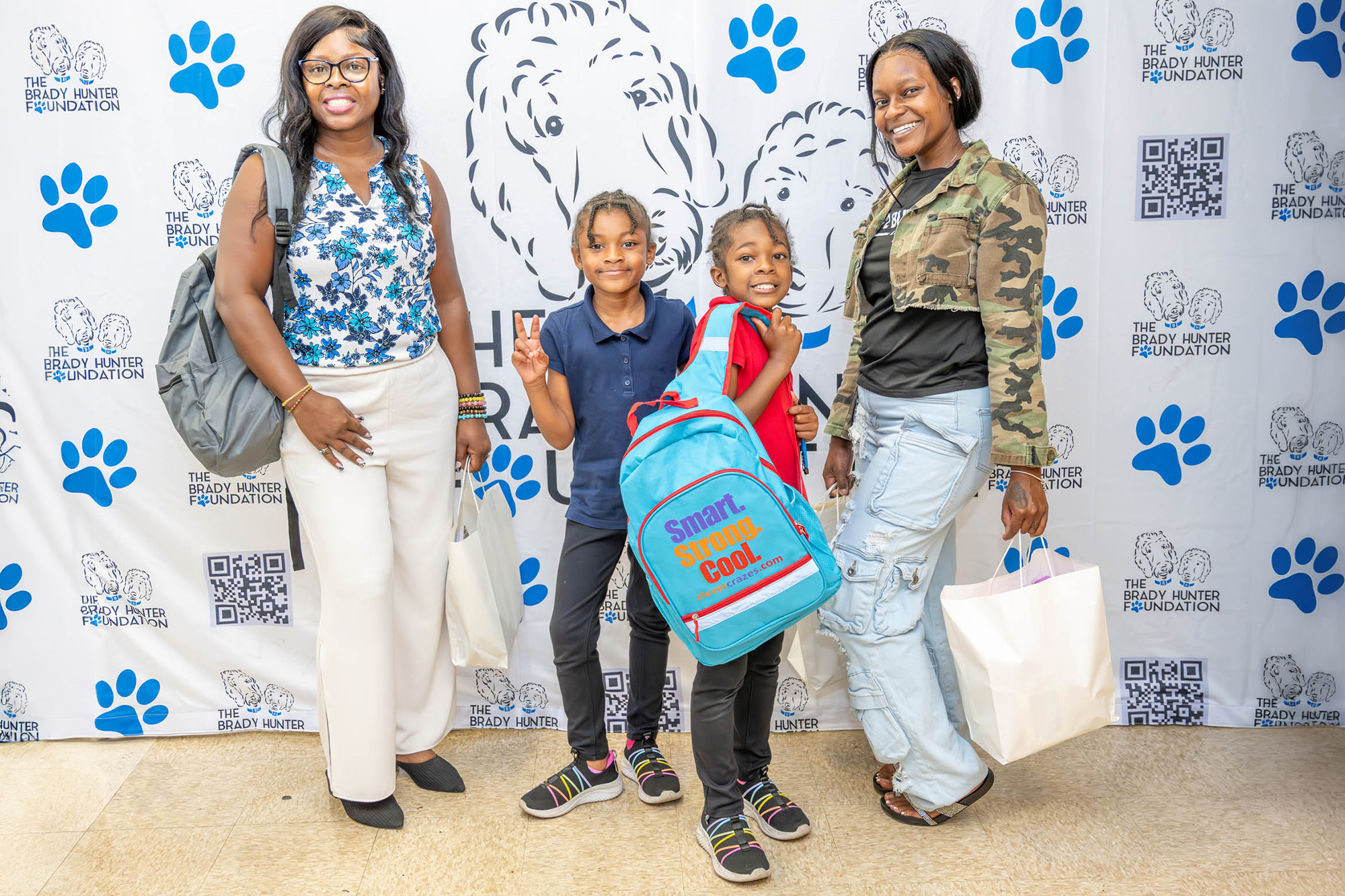 2 mothers with their children stand in front of a step and repeat