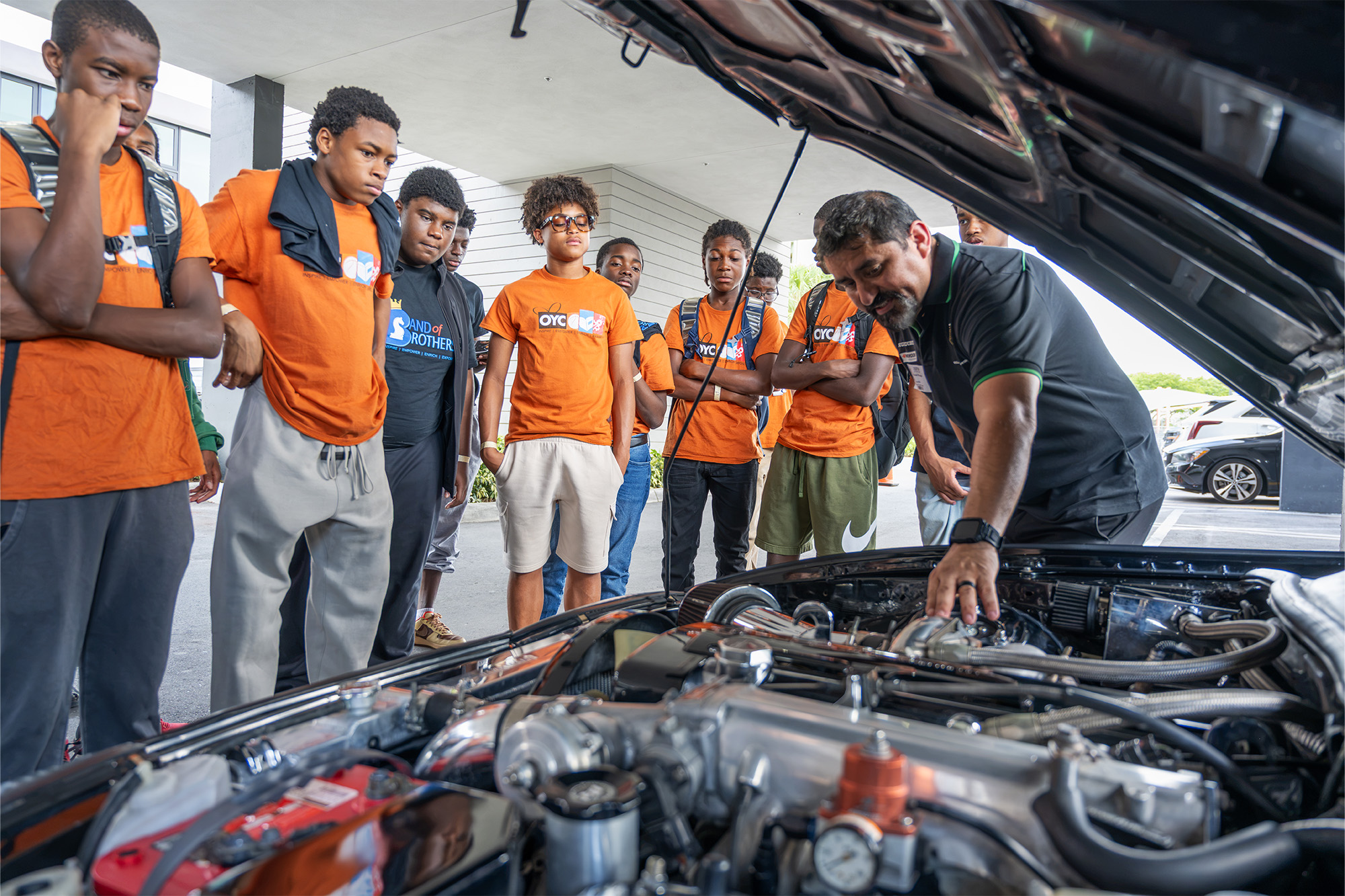 a man shows the engine of a car to a group of teenage boys